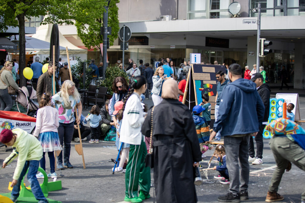 Es sind viele Menschen auf dem Bohlweg zu sehen. Kinder und Erwachsene spielen mit Stelzen, Minigolf, Kreide und Seifenblasen.