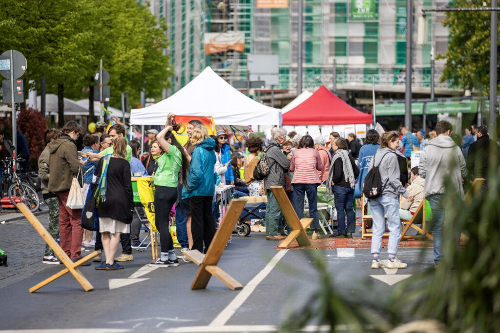EIn Bild vom Bohlweg, auf dem sich viele Menschen aufhalten. Die Menschen unterhalten sich und lachen. Es sind auch Sitzmöglichkeiten wie Stühle und Teppische zu sehen. Im Hintergrund stehen ein paar Pavillons von Initiativen, die bei der Sommerstraße beteiligt waren.