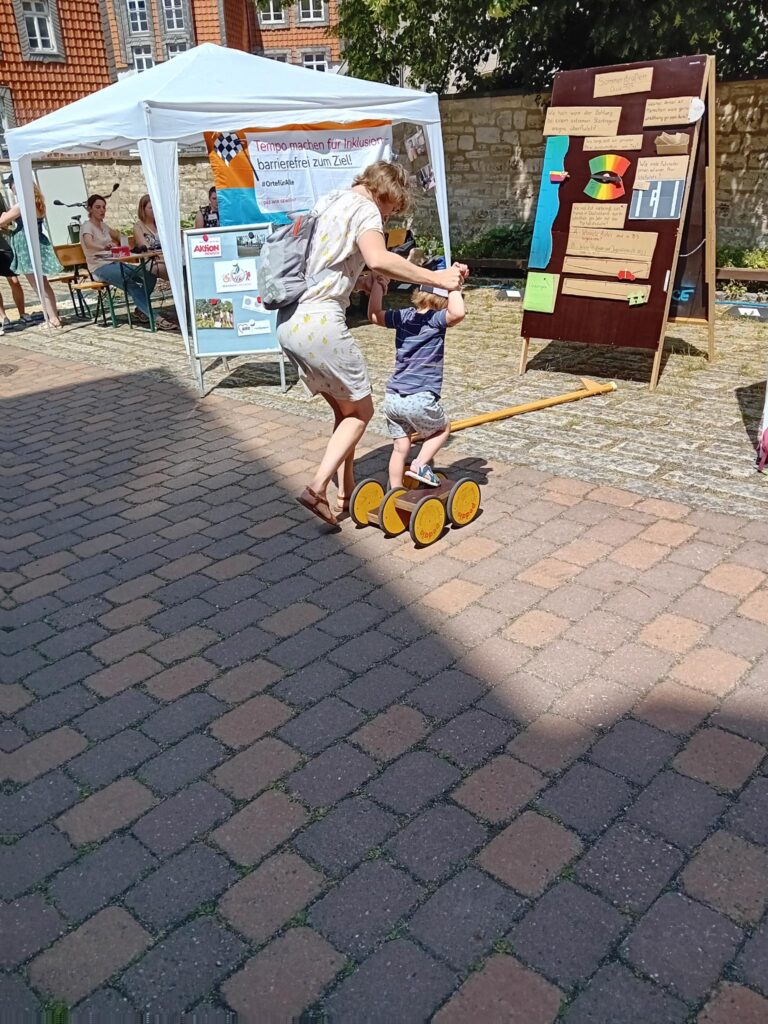In der Mitte des Bildes sind zwei Personen, eine erwachsene Person und ein Kind zu sehen. Die erwachsene Person hilft dem Kind, mit dem Pedalo zu fahren.